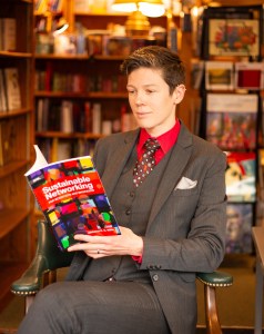 Christina sits, reading a copy of Sustainable Networking. She wears a grey suit.